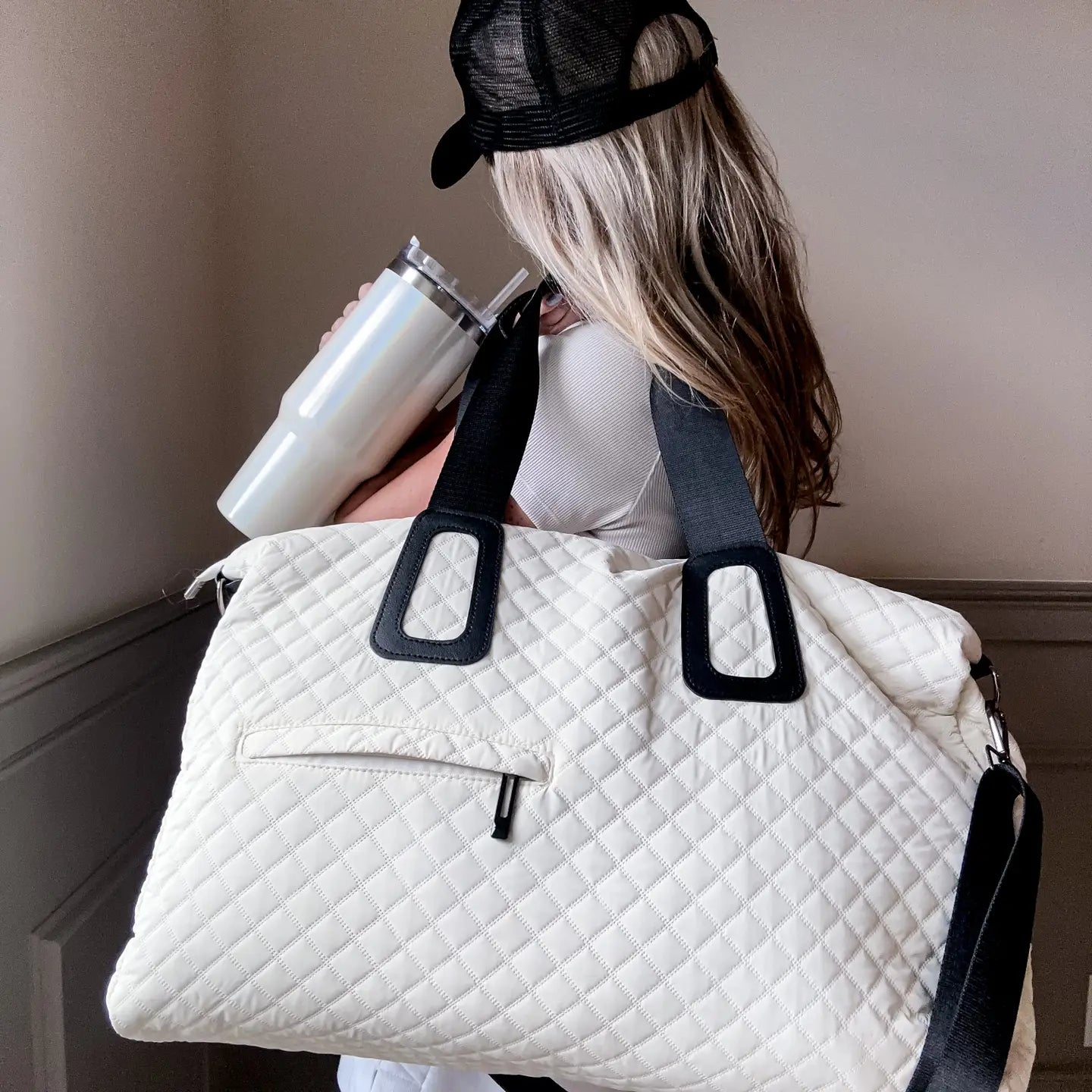 Person holding a white quilted bag with black straps and a white tumbler.