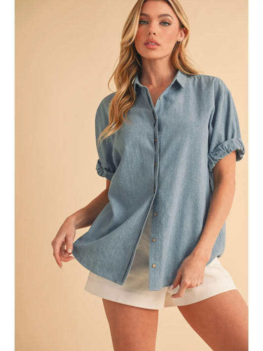 Woman wearing a light blue denim shirt over a white dress on a beige background