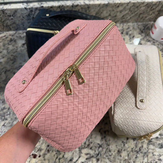 Pink woven handbag with gold zipper held by a person on a marble surface.