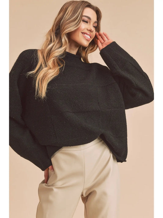 Woman wearing a black sweater and beige pants against a beige background