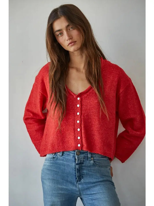 Woman wearing a red cardigan over a pink top with blue jeans against a gray background